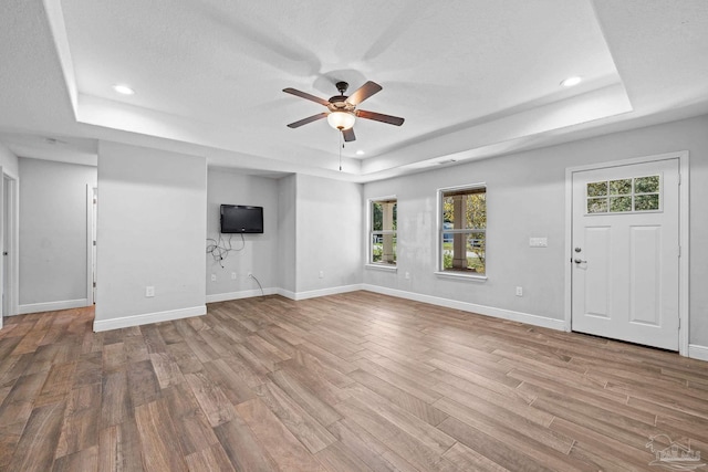 unfurnished living room featuring a textured ceiling, light wood-type flooring, a tray ceiling, and ceiling fan