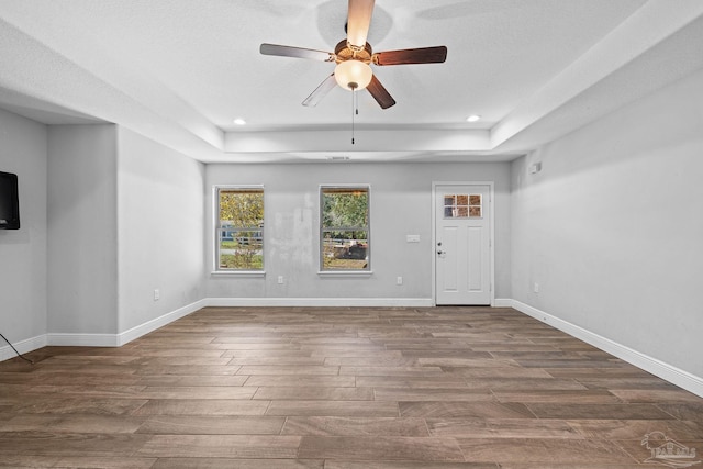 unfurnished living room featuring a raised ceiling, ceiling fan, dark hardwood / wood-style flooring, and a textured ceiling