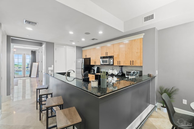 kitchen featuring a kitchen bar, dark stone countertops, black refrigerator, light brown cabinets, and kitchen peninsula