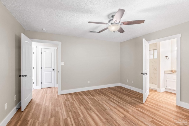 unfurnished bedroom with a textured ceiling, light wood-type flooring, ensuite bath, and ceiling fan