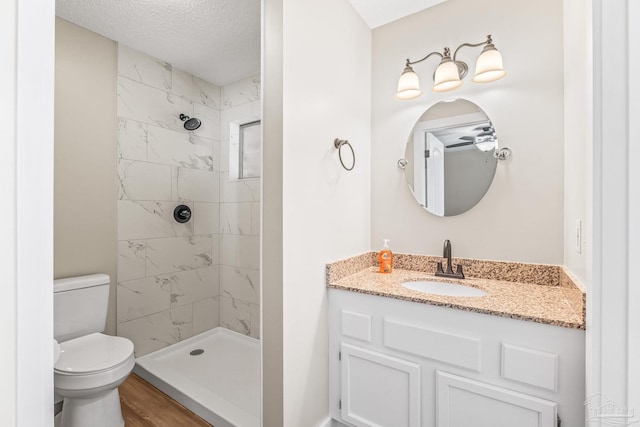 bathroom featuring a tile shower, vanity, a textured ceiling, hardwood / wood-style floors, and toilet