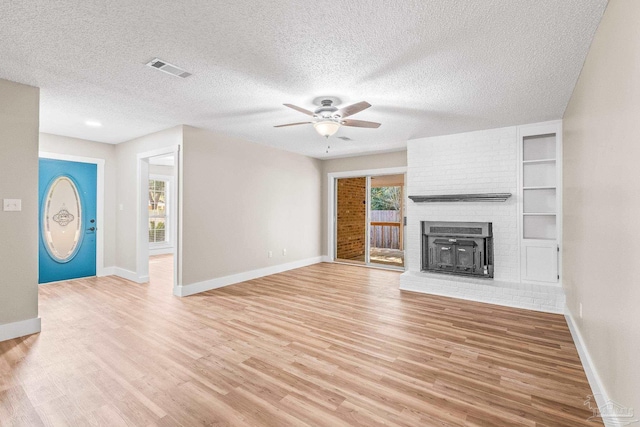 unfurnished living room with ceiling fan, a fireplace, a textured ceiling, and light hardwood / wood-style flooring