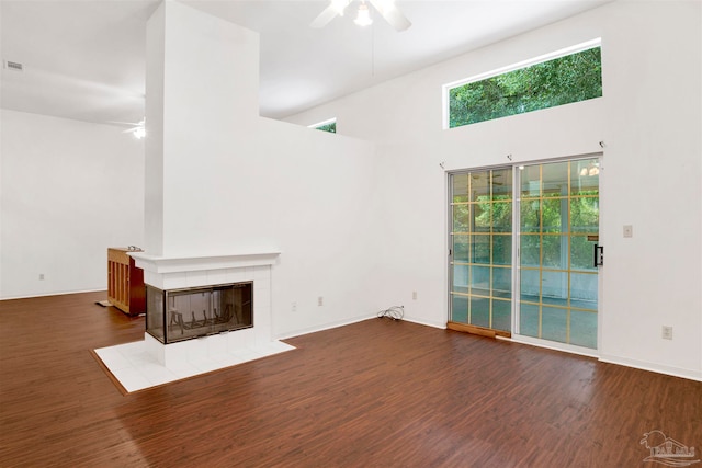 unfurnished living room with a tile fireplace, a high ceiling, dark hardwood / wood-style floors, and ceiling fan