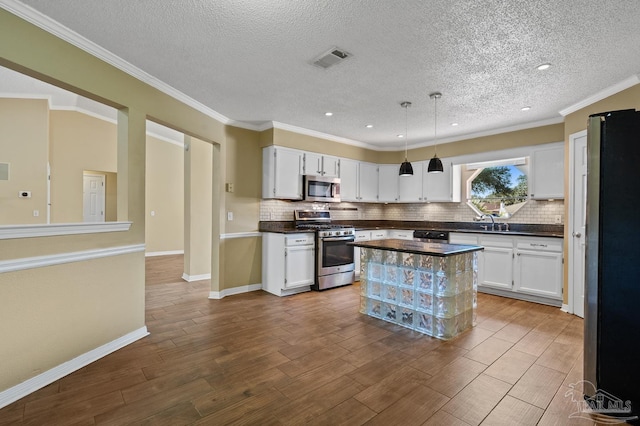 kitchen with a textured ceiling, appliances with stainless steel finishes, decorative light fixtures, white cabinetry, and ornamental molding