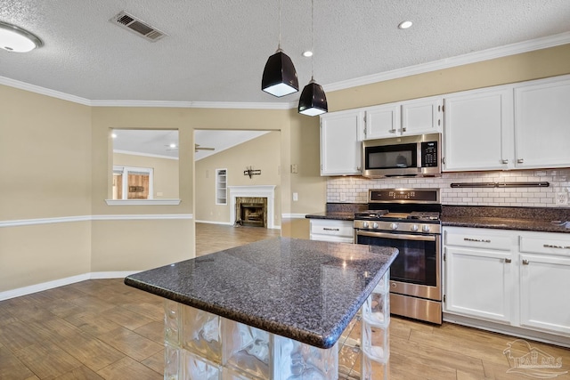 kitchen featuring a textured ceiling, white cabinets, appliances with stainless steel finishes, a kitchen bar, and hanging light fixtures