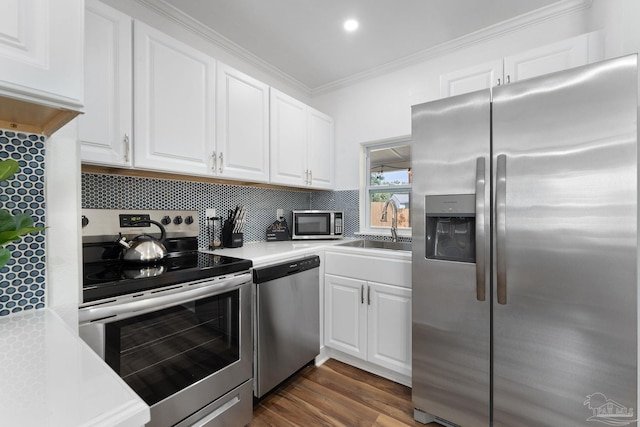 kitchen with dark wood-type flooring, appliances with stainless steel finishes, backsplash, ornamental molding, and white cabinets