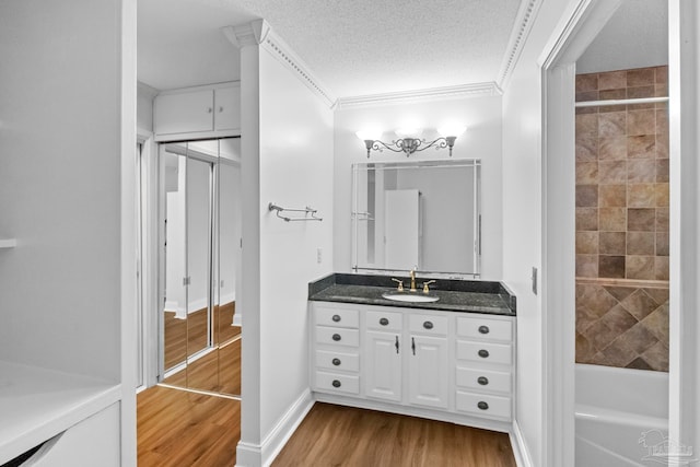 bathroom with a textured ceiling, washtub / shower combination, vanity, wood-type flooring, and ornamental molding