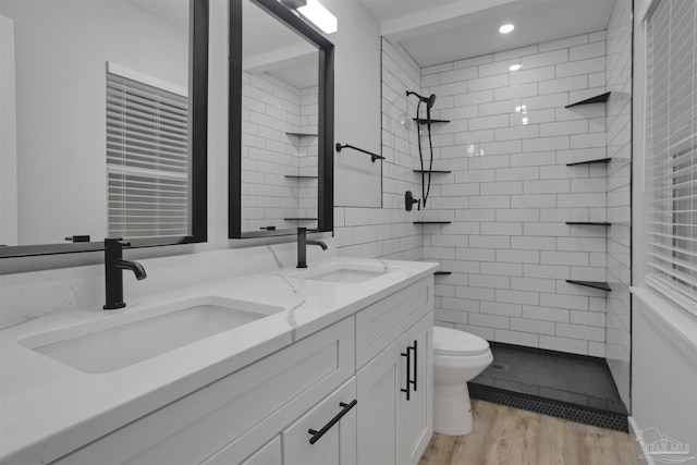 bathroom featuring a tile shower, vanity, wood-type flooring, and toilet