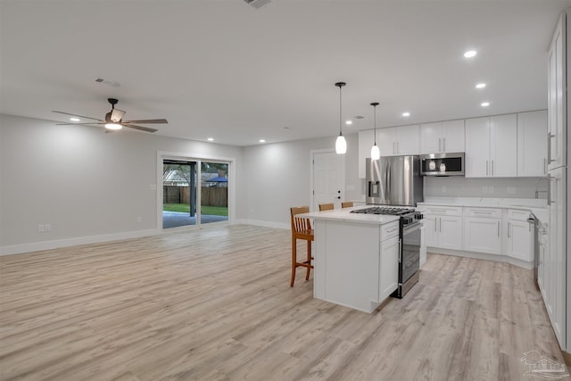 kitchen with stainless steel appliances, decorative light fixtures, white cabinets, light hardwood / wood-style floors, and a kitchen island