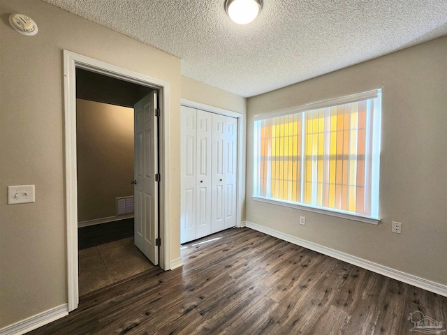 unfurnished bedroom featuring a closet, a textured ceiling, and dark hardwood / wood-style flooring