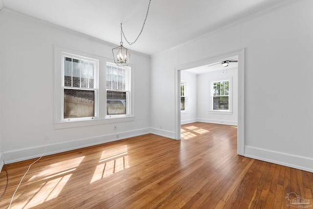unfurnished dining area with a notable chandelier, baseboards, ornamental molding, and hardwood / wood-style floors