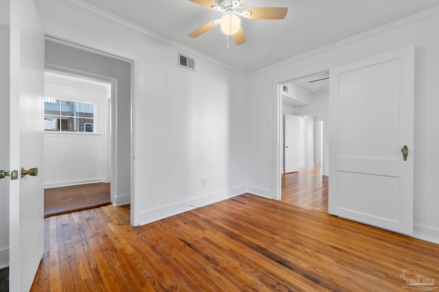 empty room with baseboards, visible vents, wood finished floors, ceiling fan, and crown molding