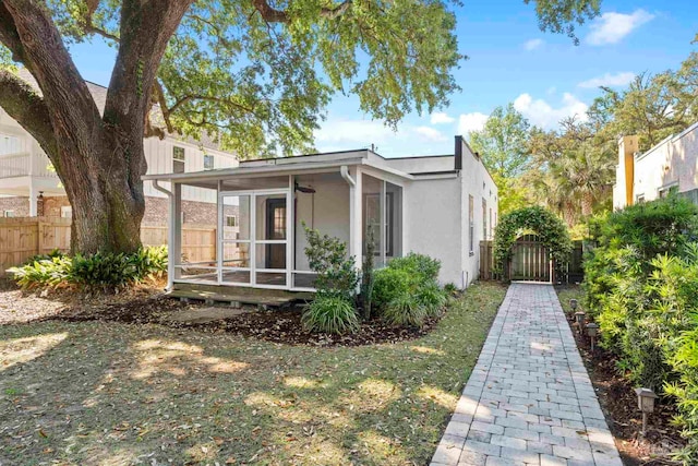 view of home's exterior with stucco siding, a sunroom, and fence