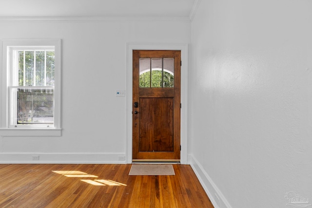 foyer featuring wood finished floors, a healthy amount of sunlight, crown molding, and baseboards
