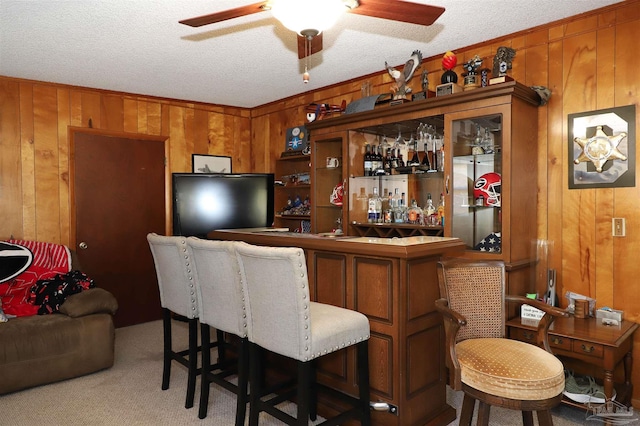 bar featuring ceiling fan, carpet flooring, a textured ceiling, and wood walls