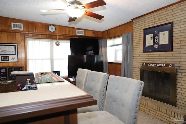 dining space featuring a fireplace, wooden walls, a textured ceiling, and ceiling fan