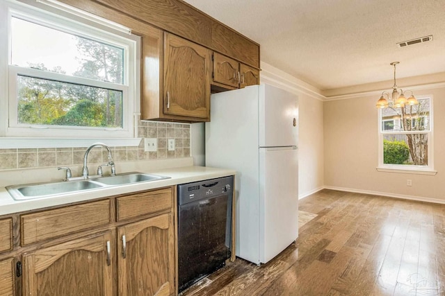 kitchen with hardwood / wood-style floors, black dishwasher, tasteful backsplash, pendant lighting, and a notable chandelier