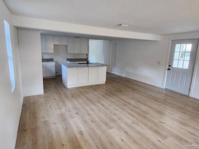 kitchen with stone counters, a kitchen island with sink, gray cabinetry, a sink, and light wood-type flooring