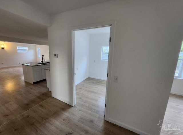 hall featuring light wood-type flooring, a sink, and baseboards