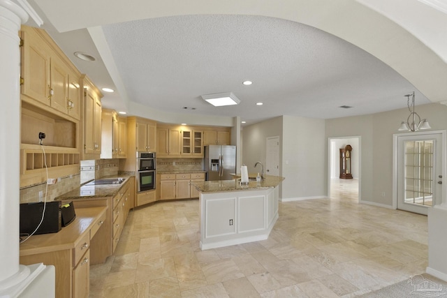 kitchen with a kitchen island with sink, stainless steel appliances, light stone countertops, decorative backsplash, and light brown cabinets