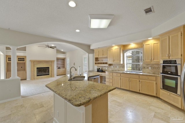 kitchen featuring appliances with stainless steel finishes, sink, light brown cabinets, light stone counters, and a center island with sink