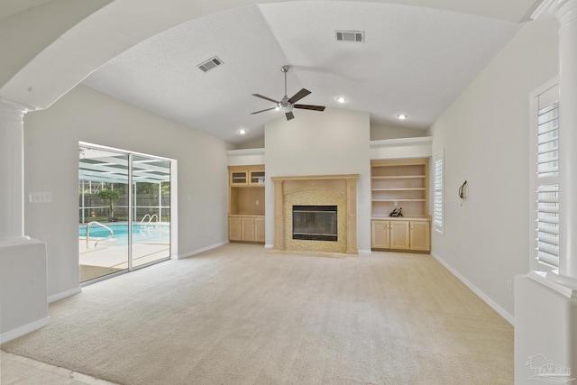 unfurnished living room featuring a premium fireplace, ceiling fan, decorative columns, vaulted ceiling, and light colored carpet