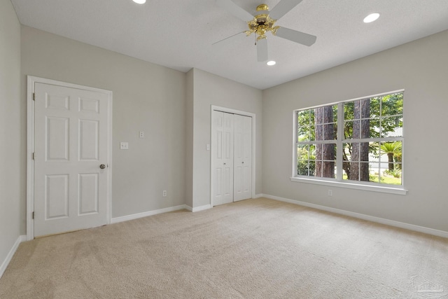 unfurnished bedroom featuring light carpet, a textured ceiling, a closet, and ceiling fan