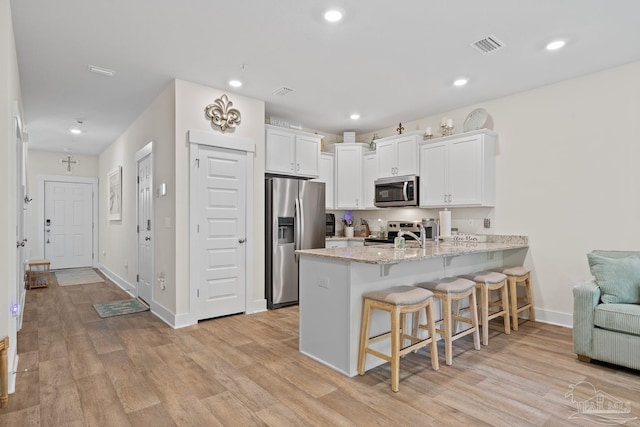 kitchen featuring appliances with stainless steel finishes, a peninsula, a kitchen breakfast bar, and light wood finished floors