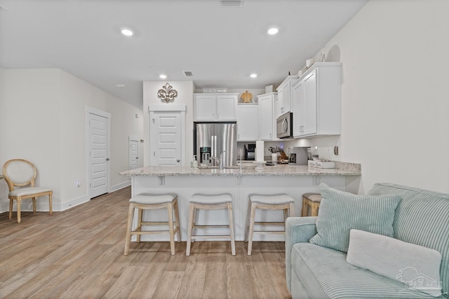 kitchen featuring stainless steel appliances, a peninsula, white cabinets, open floor plan, and light wood-type flooring