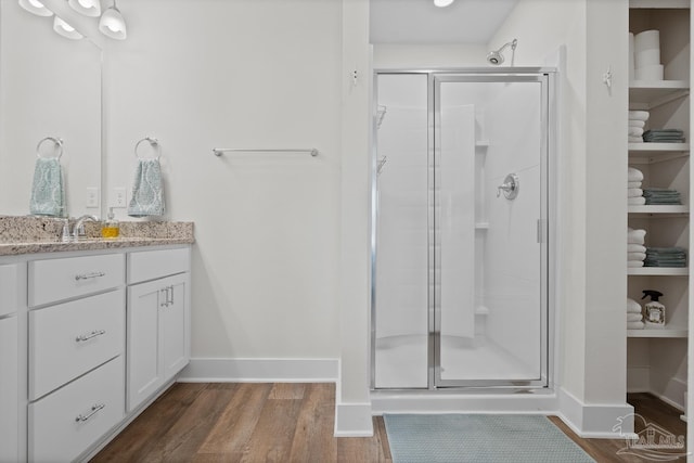 bathroom with wood finished floors, a shower stall, vanity, and baseboards