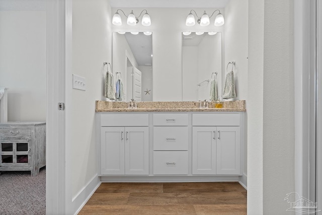 bathroom featuring double vanity, baseboards, a sink, and wood finished floors