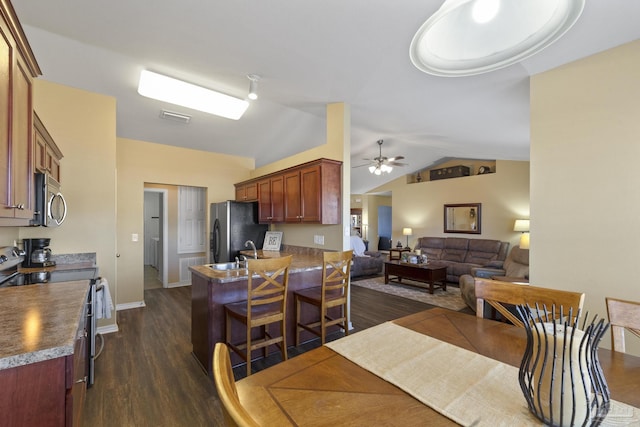 interior space featuring a kitchen breakfast bar, vaulted ceiling, ceiling fan, dark hardwood / wood-style flooring, and stainless steel appliances