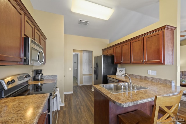 kitchen with kitchen peninsula, sink, dark wood-type flooring, a kitchen bar, and stainless steel appliances