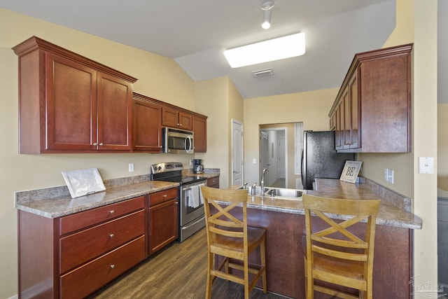 kitchen featuring appliances with stainless steel finishes, a kitchen bar, dark wood-type flooring, sink, and vaulted ceiling