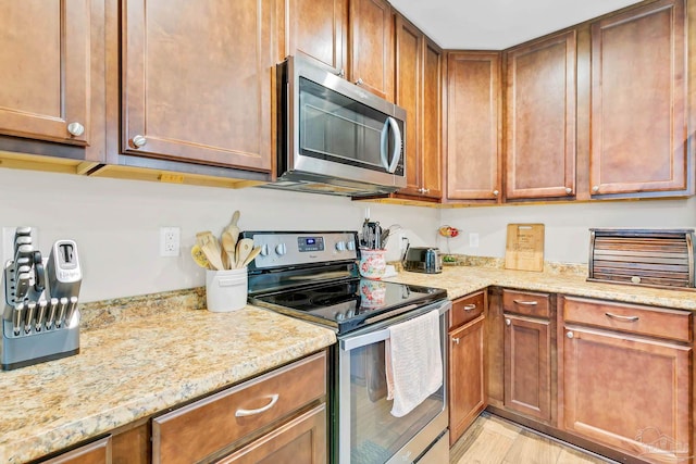 106 W Meadow Dr, Atmore, AL 36502 - kitchen featuring stainless steel appliances, brown cabinets, light stone countertops, and light wood finished floors
