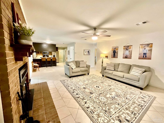 living room featuring ceiling fan, light tile patterned floors, and a brick fireplace