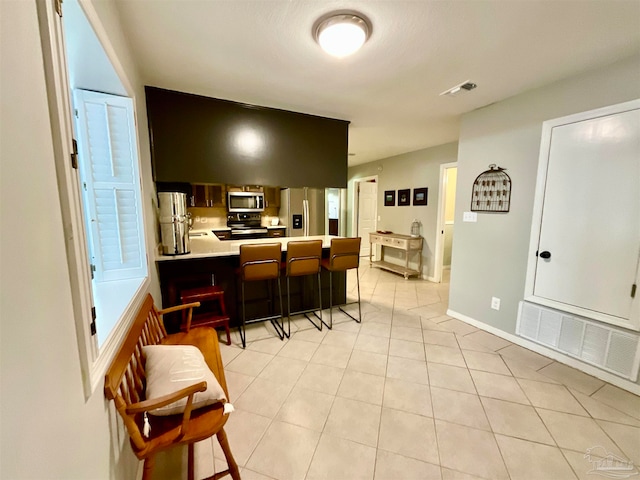 kitchen with a kitchen breakfast bar, kitchen peninsula, stainless steel appliances, and light tile patterned floors