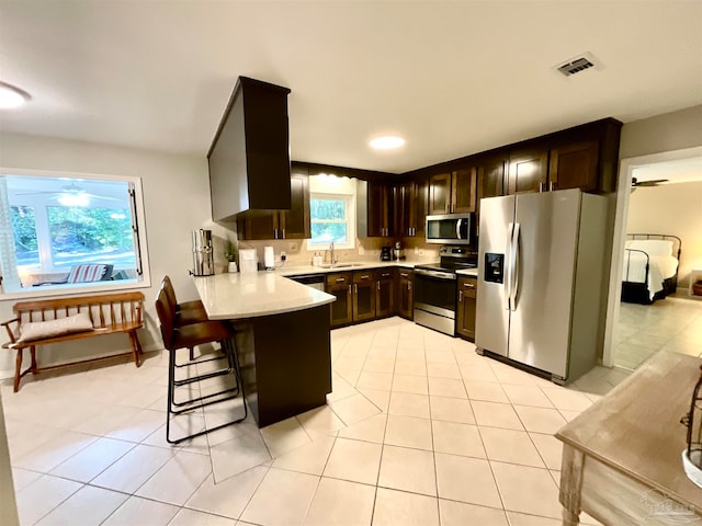 kitchen featuring sink, light tile patterned floors, appliances with stainless steel finishes, kitchen peninsula, and a breakfast bar area