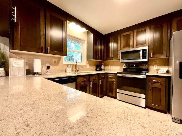 kitchen with light stone countertops, sink, backsplash, dark brown cabinets, and appliances with stainless steel finishes