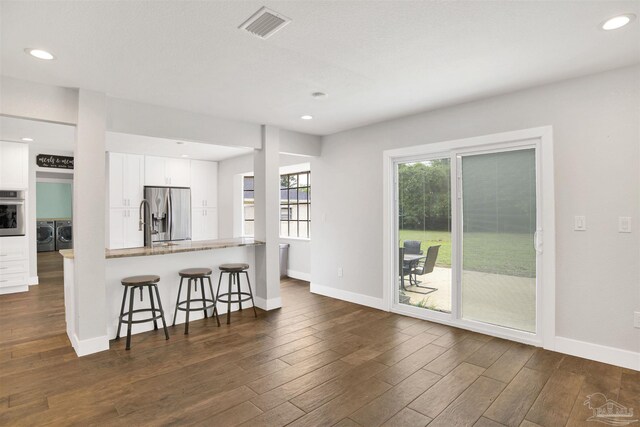 9852 Hillview Dr, Pensacola, FL 32514 - kitchen with stainless steel appliances, washing machine and dryer, a kitchen breakfast bar, white cabinets, and dark wood-style floors