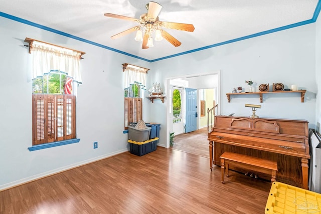living area with wood finished floors, ornamental molding, baseboards, and a ceiling fan