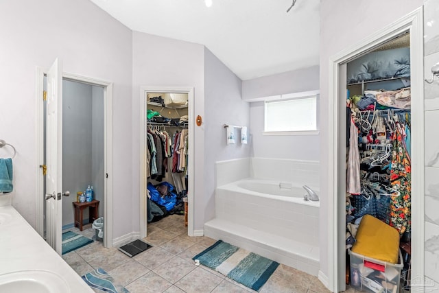 full bath featuring a walk in closet, a garden tub, tile patterned flooring, and lofted ceiling