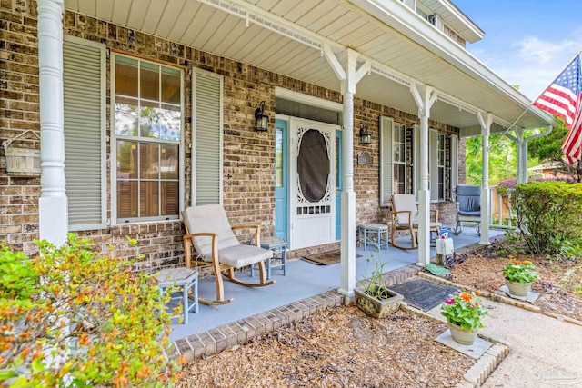 view of exterior entry with brick siding and covered porch