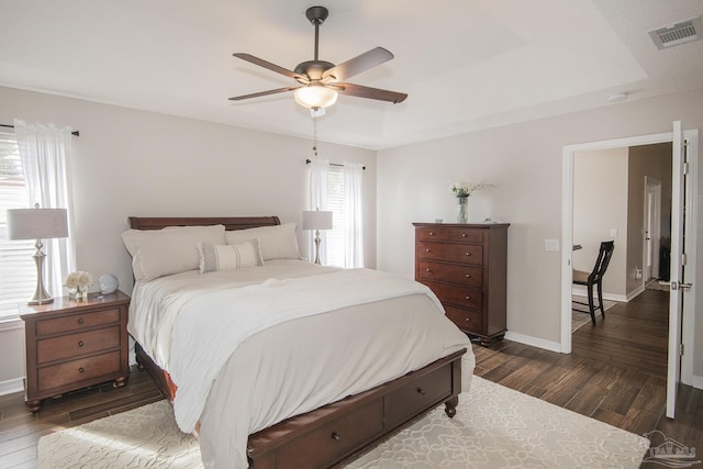 bedroom featuring baseboards, visible vents, dark wood finished floors, and a raised ceiling