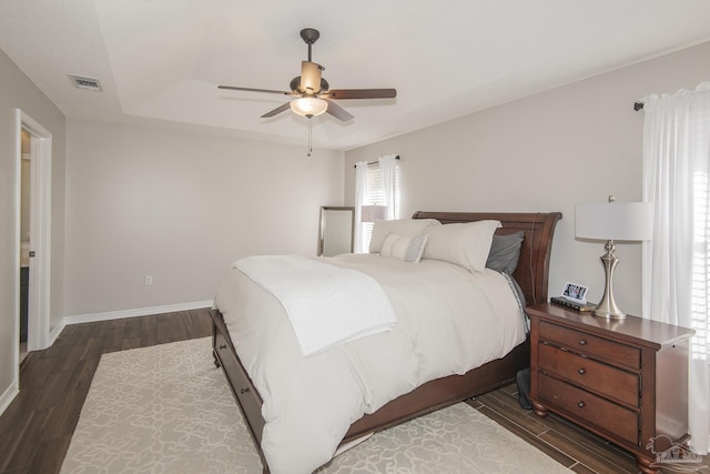 bedroom featuring a raised ceiling, visible vents, ceiling fan, wood finished floors, and baseboards