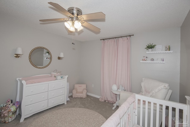 carpeted bedroom featuring a nursery area, baseboards, a ceiling fan, and a textured ceiling