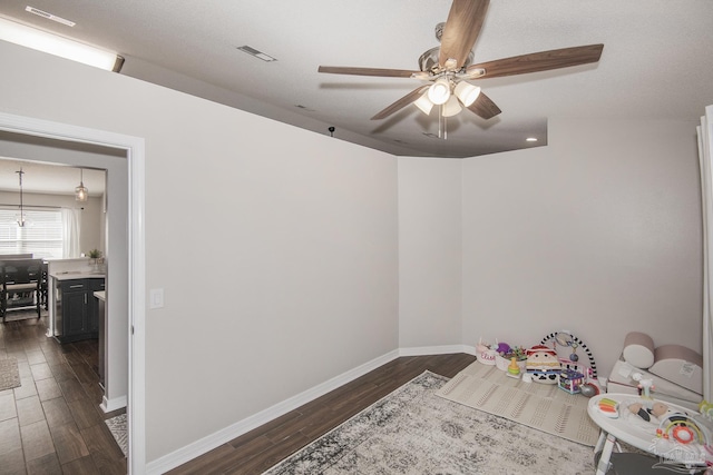 game room with dark wood-type flooring, a ceiling fan, visible vents, and baseboards