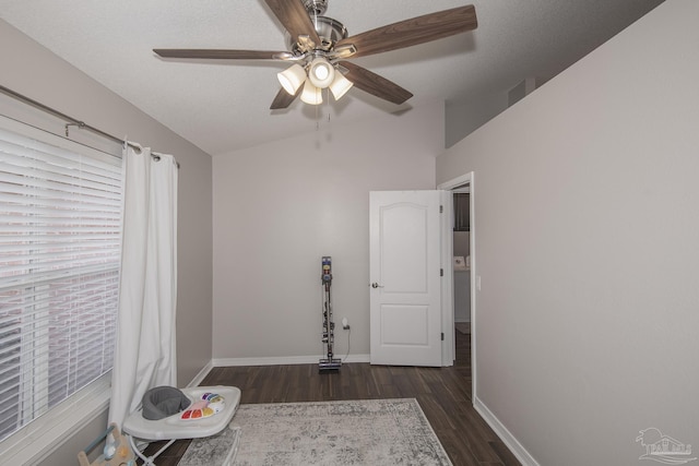 interior space with baseboards, ceiling fan, dark wood-style flooring, vaulted ceiling, and a textured ceiling