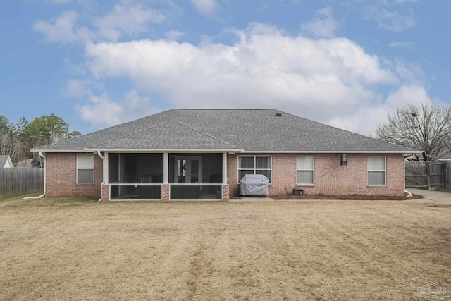 rear view of property with a shingled roof, a sunroom, fence, and a lawn