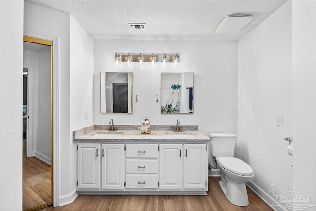 2574 1st Ct, Navarre, FL 32566 - bathroom featuring toilet, double vanity, baseboards, wood finished floors, and a textured ceiling